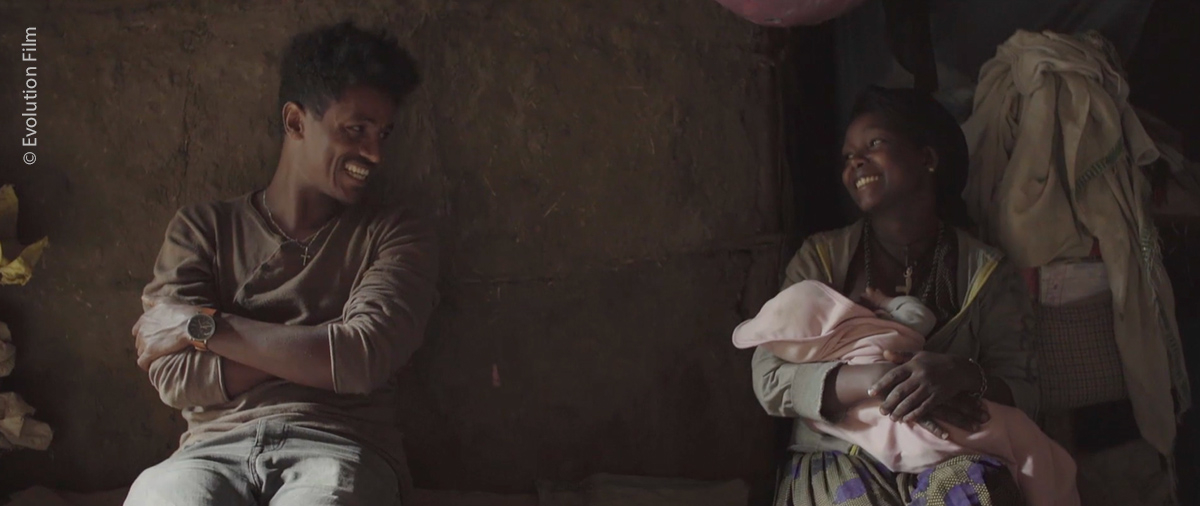 Filmstill aus Among us Women: junge Frau mit Neugeborenen, freut sich. Neben ihr sitzt ein Mann.