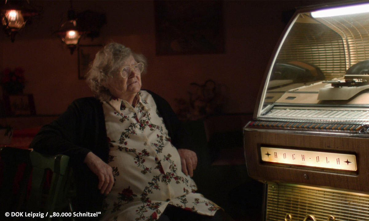 Filmstill "80.000 Schnitzel", abgebildet ist eine alte Frau vor einer Jukebox