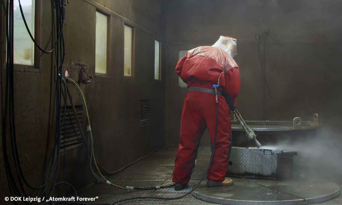 Filmstill "Atomkraft forever", abgebildet ist ein Mensch in Schutzbekleidung beim Saubermachen