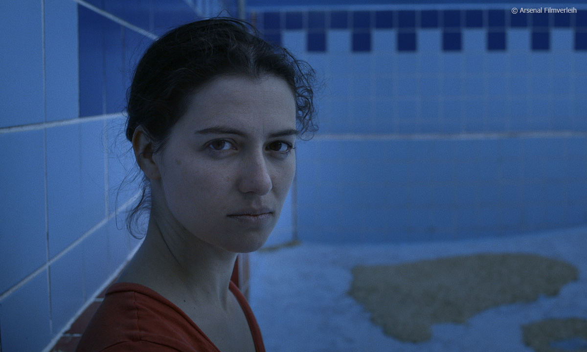 Filmstill aus "Swimmingpool am Golan". Zu sehen ist eine Frau, die in einem leeren Swimmingpool steht.