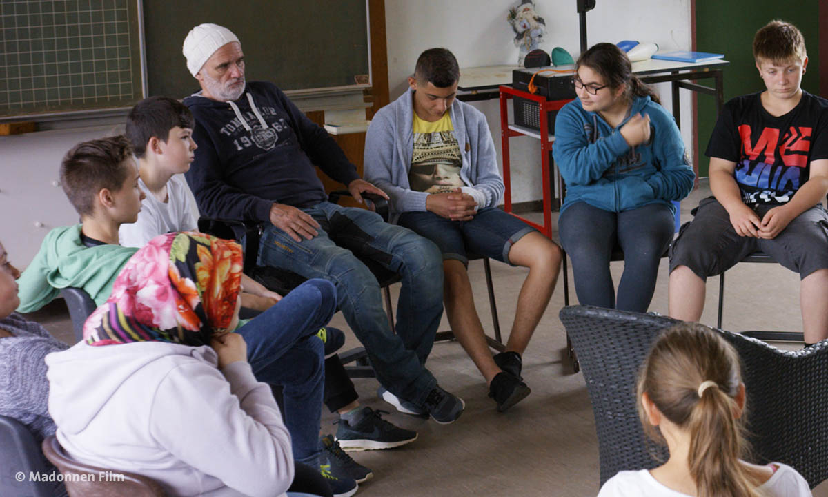 Filmstill aus "Herr Bachmann und seine Klasse". Zu sehen ist der Lehrer mit Schülerinnen und Schülern.