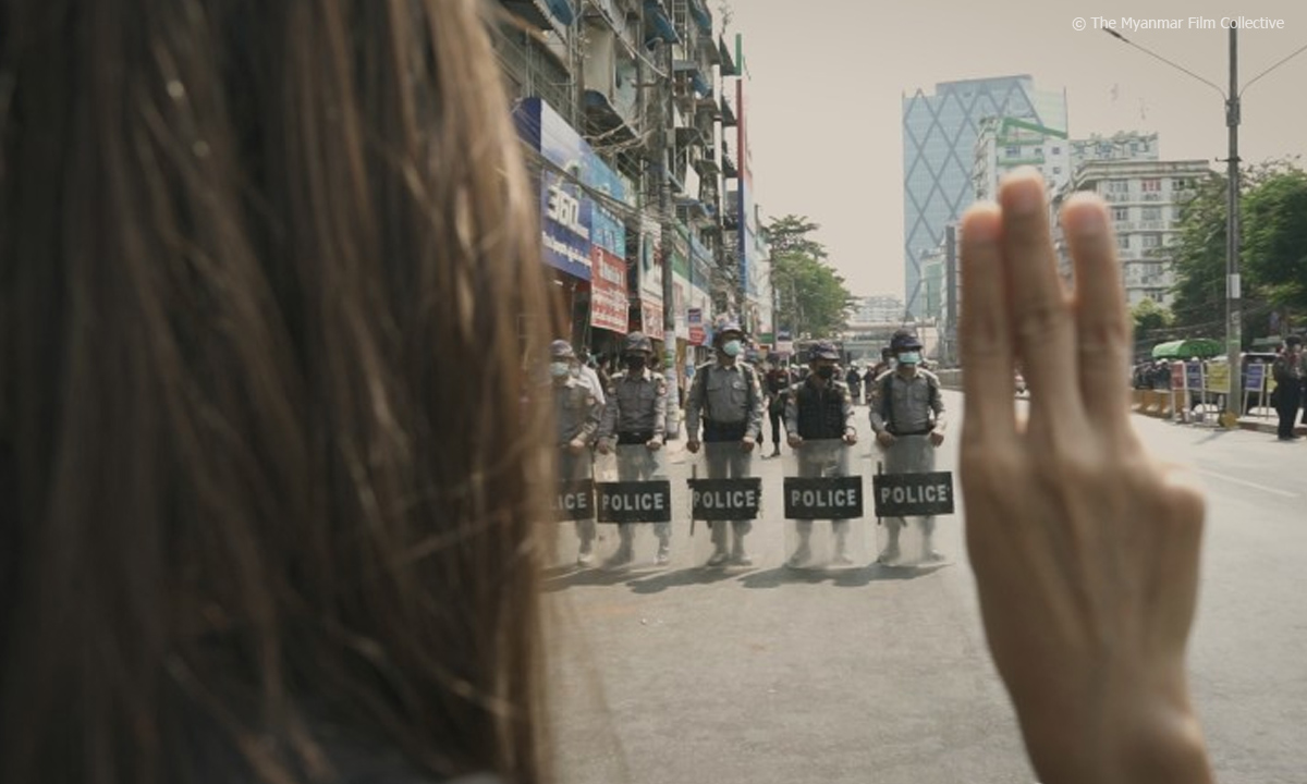 Filmstill aus "Myanmar Diaries". Zu sehen ist eine friedlich protestierende Frau, die sich bewaffneten Männern gegenübersieht.