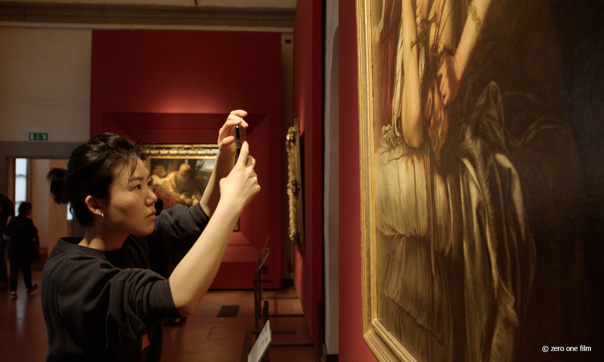 Foto einer jungen asiatisch aussehende Frau, die mit ihrem Smartphone in den Uffizien ein Gemälde ablichtet